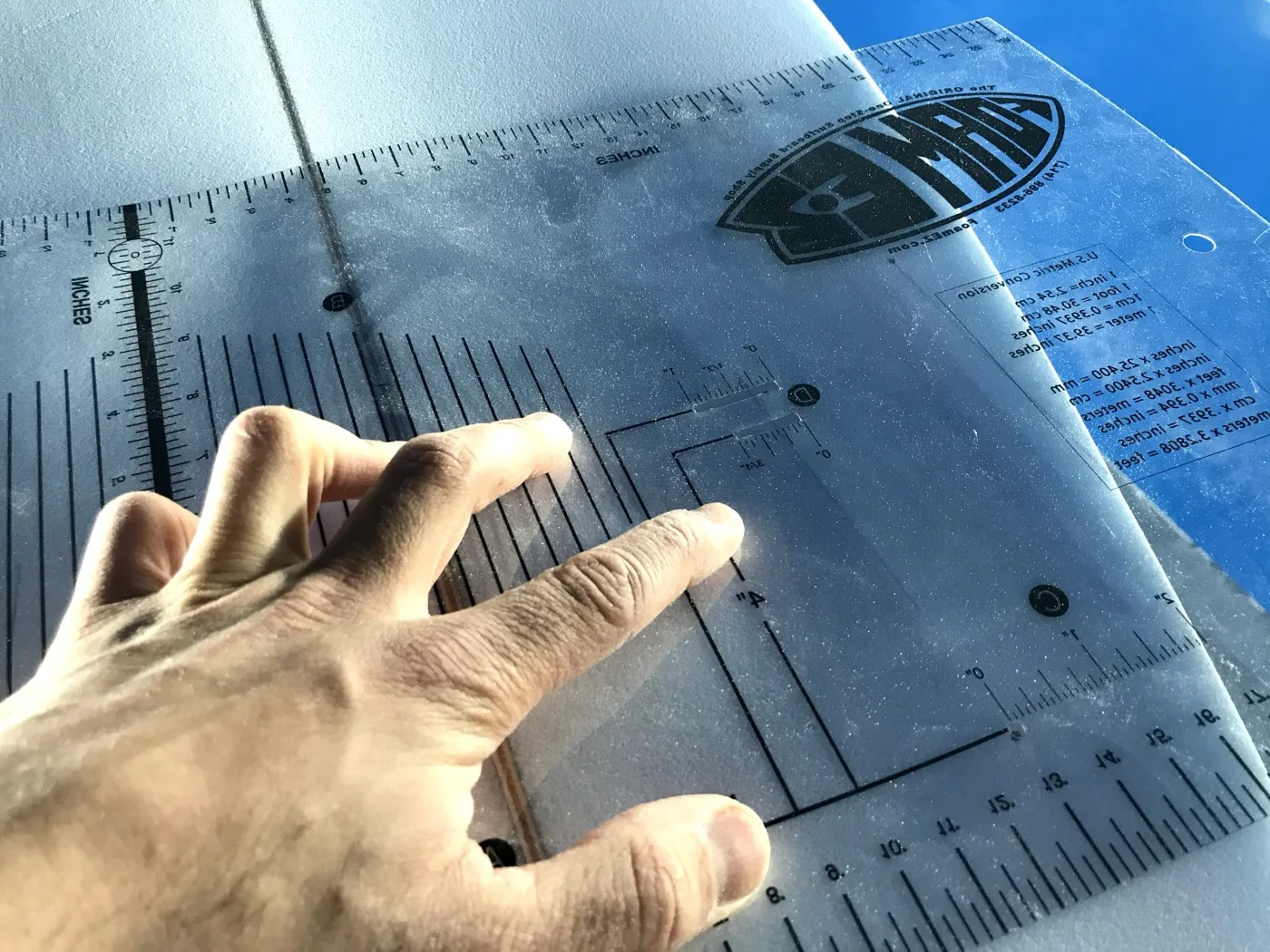 Shaper’s hands checking a board template against a blank